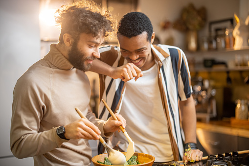 Two guys of different ethnicity having fun while making salad together on kitchen. Concept of gay couples and everyday life at home . Caucasian and hispanic man cooking healthy food