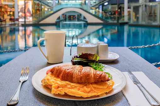 Cup of coffee with a croissant and egg sandwich at breakfast at a cafe in a luxury shopping center with high-end restaurants and shops in Singapore