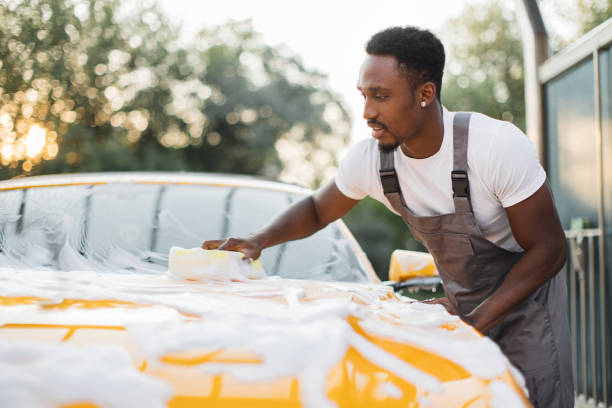 junger attraktiver afrikaner, der sein modernes luxusauto wäscht - autowaschanlage stock-fotos und bilder