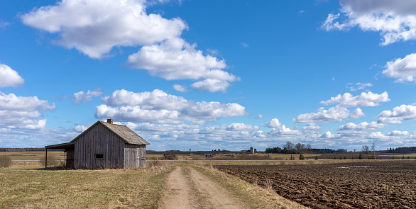 An old abandoned small wooden house in the field blue sky white clouds, next to a path barn or scary concept.