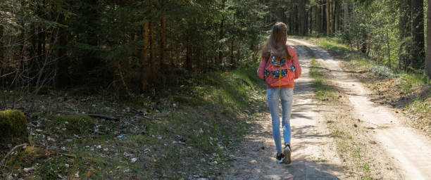 istock One young girl tourist with backpack walking on path through forest during summer day. Panoramic view. 1369073957