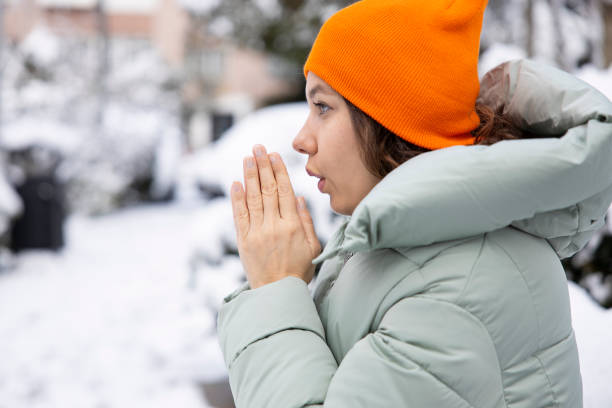 young woman warming her hands on the street in snowy cold day - congelação imagens e fotografias de stock