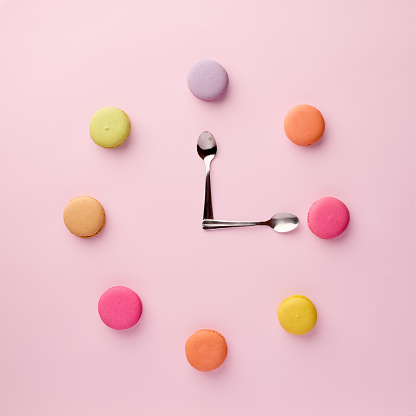 A clock made of pastel colored macarons and teaspoons. Snack time concept.