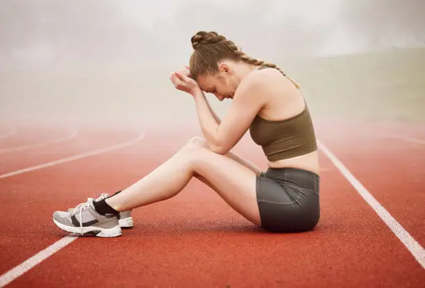 Photo of Full length shot of an attractive young female athlete looking dejected while sitting on the track after a race