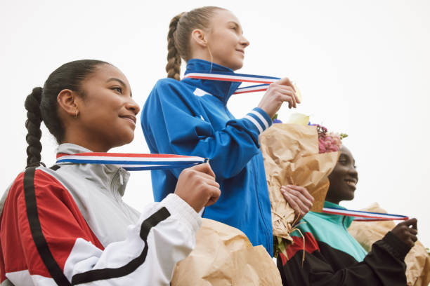 foto recortada de tres atractivas jóvenes atletas celebrando sus logros en el podio - medallista fotografías e imágenes de stock