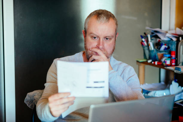 worried man checking bills at home - expense imagens e fotografias de stock