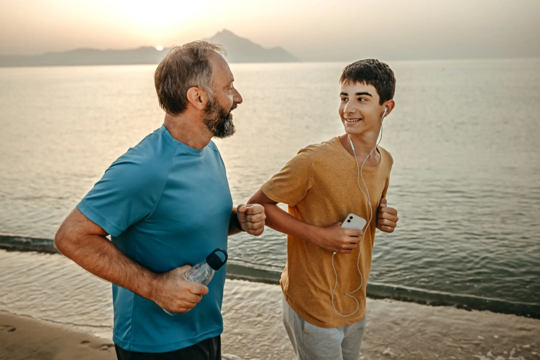 Smiling father and son jogging at beach during sunset