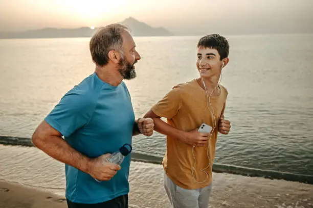 Photo of Smiling father and son jogging at beach during sunset