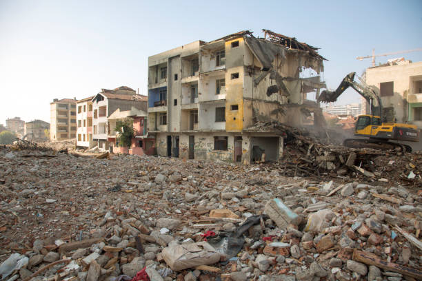 Istanbul, Turkey - November 8, 2021: Building demolition works in the urban transformation zone. Excavator vehicle, abandoned buildings ready for demolition among piles of dust and rubble. Horizontal shot with blue sky in the background. Istanbul city, Kadikoy district, Fikirtepe region.