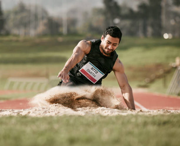 Full length shot of a handsome young man competing in a long jump event outside Stick the landing long jump stock pictures, royalty-free photos & images