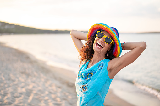 Portrait of a smiling woman with colorful hat, enjoying the day on the beach, posing during golden hour