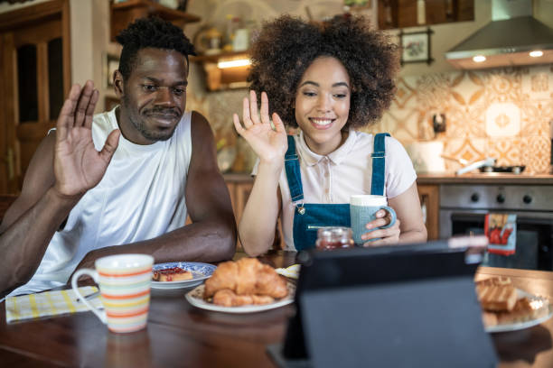 istock Friendly young afro american couple having video call using digital tablet. Smiling young black spouses join online conversation, waving hands to webcam while sitting in their kitchen. 1369085059