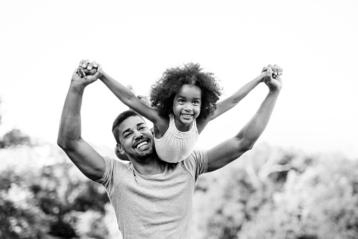 Portrait of happy african american father carrying daughter on back outdoors. Family happiness love concept.