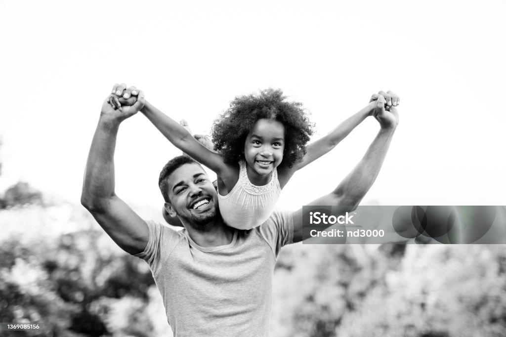 Portrait of happy black father carrying daughter on back outdoors. Family happiness love concept. Portrait of happy african american father carrying daughter on back outdoors. Family happiness love concept. Black And White Stock Photo