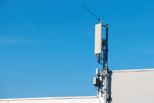 Cellular phone signal repeater antenna mounted on top of industrial building with blue sky as copy space