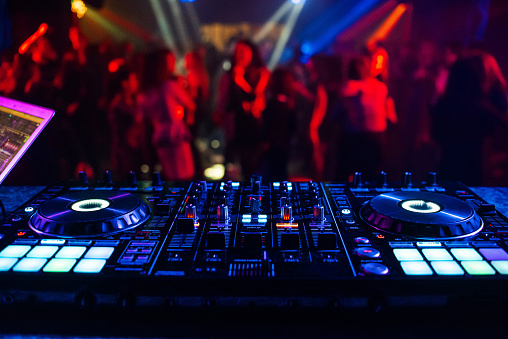 music controller DJ mixer in a nightclub at a party against the background of blurred silhouettes of dancing people