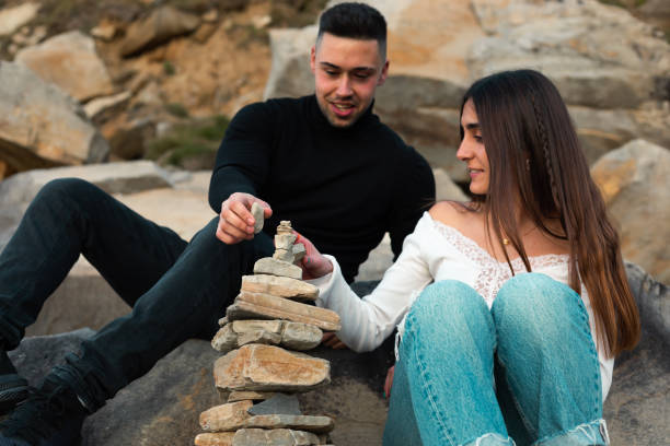 Young caucasian couple building a rock tower on the beach.