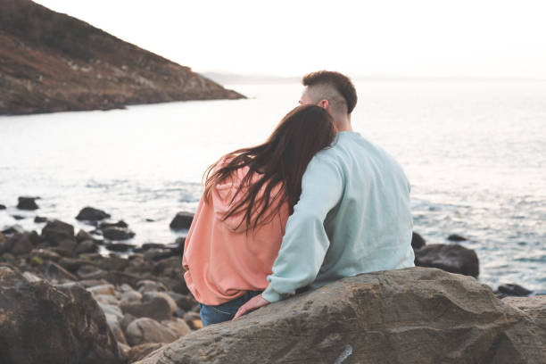 istock Young caucasian woman and man embracing each other at a rocky beach while sunset. 1369088603