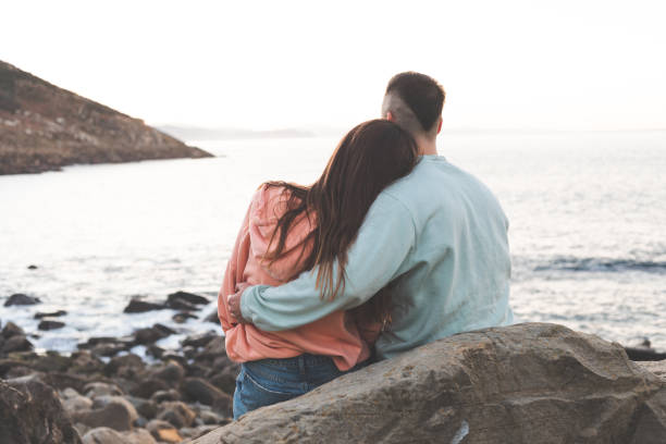 istock Young caucasian woman and man embracing each other at a rocky beach while sunset. 1369088607