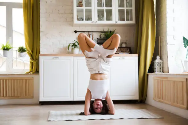 young woman doing yoga and  headstand  in room at home. home fitness, activewear. Healthy and sport lifestyle.