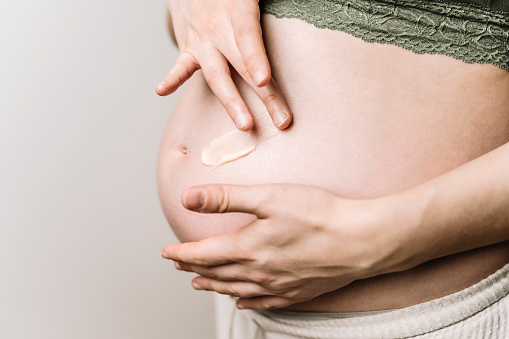 A pregnant woman uses a cream for stretch marks. Prevention of stretch marks on the abdomen and legs, skin care during pregnancy. High quality photo
