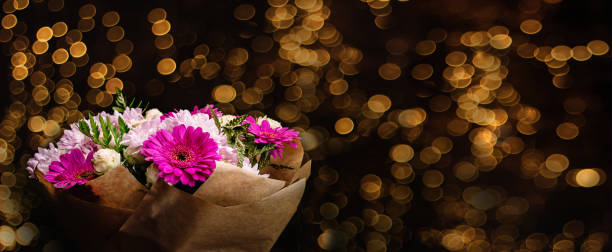 grand beau bouquet de chrysanthèmes, gerberas, roses et fougères aux couleurs rose et violet, emballé dans du papier artisanal brun et isolé sur un fond noir avec du bokeh doré. bannière de carte postale - golden daisy flash photos et images de collection