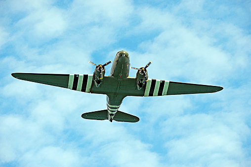 Historic Dakota troop transport flying over English Channel, England.  Douglas DC3 Dakota twin propeller engine troop transport and freight aircraft in D-Day colour scheme in level flight overhead Poole Bay, English Channel, England in fluffy cloudscape blue,sky