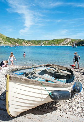 Holidaymakers enjoy the shingle beach at Lulworth Cove, West Dorset, England. Lulworth Cove is a world famous bay created by a breaching of the limestone cliffs and chalk land mass behind, also known for its unique geology and landforms, including the Lulworth Crumple and Stair Hole, formed by the sea and a river swollen by melting ice at the end of the last Ice Age