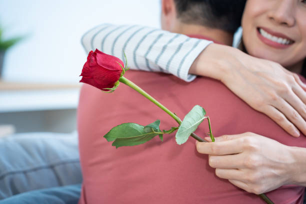 asiatischer junger mann überrascht und gibt rosenblumen an schöne freundin. attraktives romantisches neues ehepaar mann und frau verbringen zeit, um jubiläum und valentinstag zusammen im haus zu feiern. - rose family stock-fotos und bilder