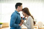 アジアの若者は驚き、美しいガールフレンドにバラの花を与えます。魅力的なロマンチックな新しい結婚カップル男性と女性は家の中で一緒に記念日とバレンタインデーを祝うために時間を�