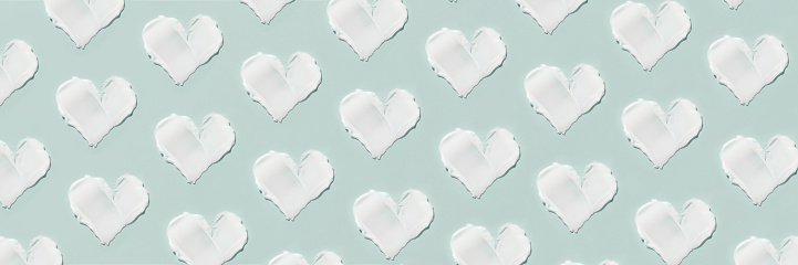 Smears of cosmetic cream in the shape of a heart on a blue background. Pattern.