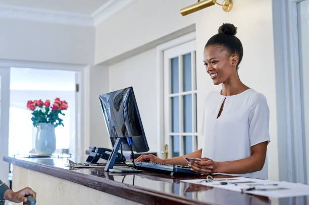 aufnahme einer attraktiven jungen frau, die in der rezeption eines hotels steht und den computer benutzt - hotel reception hotel receptionist health spa stock-fotos und bilder