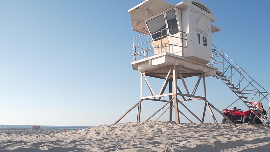 Lifeguard stand or life guard tower hut, surfing safety on California beach, USA. Summer pacific ocean aesthetic. Rescue station, coast lifesavers wachtower or house on sand. Red ATV on Mission beach.