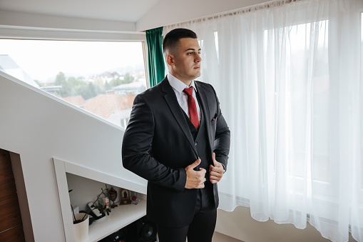 Handsome young man dressing himself at home, front view