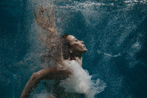 Portrait of beautiful swimming and diving woman in bridal dress underwater with bubbles.