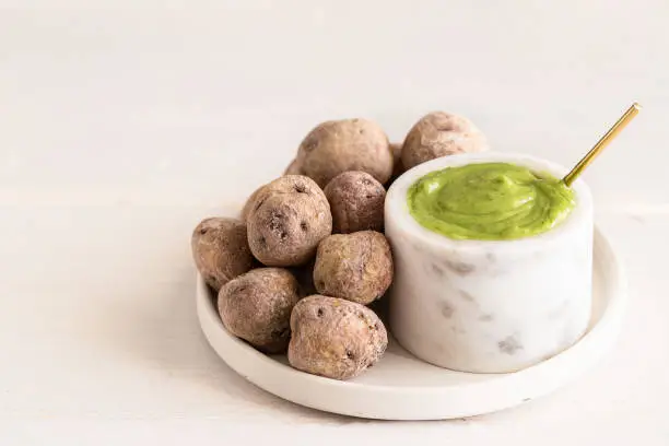 Photo of Local Canary Islands dish, Papas Arrugadas (wrinkly potatoes) with Mojo verde green sauce) on white plate on restaurant table.