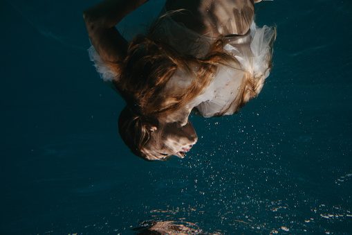 Portrait of beautiful swimming and diving woman in bridal dress underwater.
