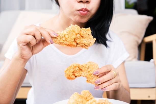 wanita asia lebih dari makan berminyak, junk food tangan memegang ayam goreng closeup - makan banyak potret stok, foto, & gambar bebas royalti