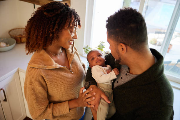 istock Smiling parents looking down at their baby while standing in their kitchen 1369111224