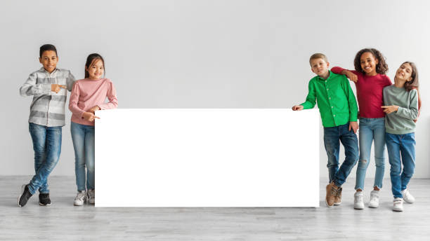 szczęśliwe różnorodne dzieci stojące w pobliżu białej tablicy na szarym tle - caucasian white poster little boys zdjęcia i obrazy z banku zdjęć