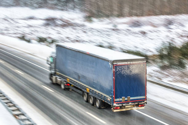 Semi-trailer truck on a slippery and dangerous highway through the Veluwe forest in Gelderland, The Netherlands, during a snow blizzard in winter