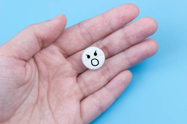 istock Pill with a screaming emoticon in hand on a blue background. Painkiller concept 1369114049