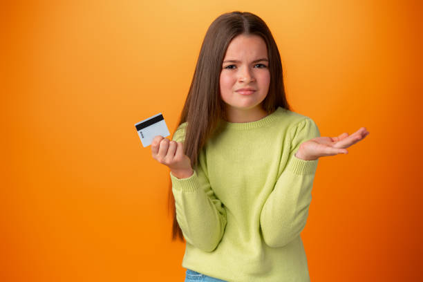 teen girl holding credit card clueless and confused against orange background - blank expression head and shoulders horizontal studio shot imagens e fotografias de stock