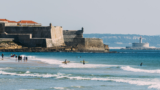 Carcavelos Beach, Portugal - February 5, 2022: Surfers at Carcavelos beach, Lisbon Region, Portugal with historic fort in the background