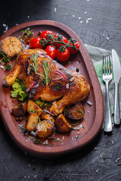 istock Oval wooden tray, kitchen cutting board, fried chicken, thighs with vegetables, fried potatoes, spices and vegetables, dark and moody, clouseup on a black isolated background 1369117280