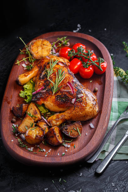 istock Oval wooden tray, kitchen cutting board, fried chicken, thighs with vegetables, fried potatoes, spices and vegetables, dark and moody, clouseup on a black isolated background 1369117281