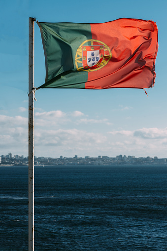 Portuguese flag with Cascais, Portugal in the background next to the sea on the Portuguese Riviera. Portugal is a country in south-western Europe