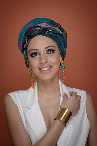 Beautiful woman in a turban.Young beautiful woman with turban and golden accessories.Beauty fashionable woman with hairs wrapped in turban. Pretty Caucasian model wearing  earrings  posing in studio.