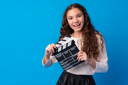 Smiling girl holding clapper board against blue background, close up