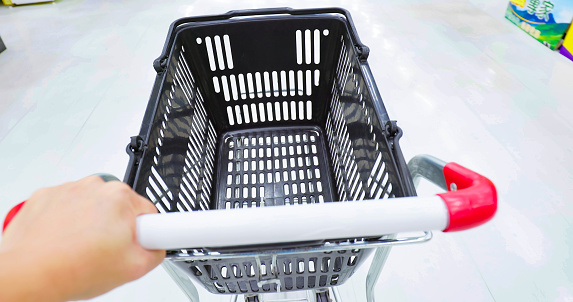 close up of asian woman hold empty shopping cart in grocery store or supermarket